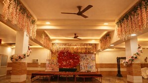 A hall with a central altar decorated with flowers and religious paintings, flanked by pillars and a ceiling fan. - Hotel Midway Taj (Agra)