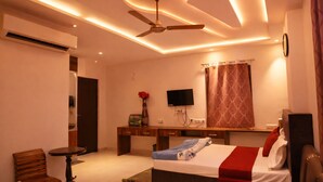A hotel room with a bed, desk, chair, TV, and ceiling fan. - Hotel Midway Taj (Agra)