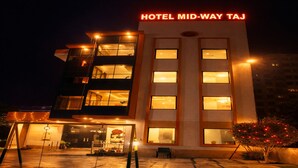 A hotel with a modern design, featuring a prominent sign reading "HOTEL MID-WAY TAJ". The building has multiple floors with large windows, and the entrance is accessible via a covered walkway. - Hotel Midway Taj (Agra)