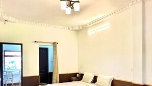 A hotel room with a bed, a chair, a small table, and a door leading to a balcony.