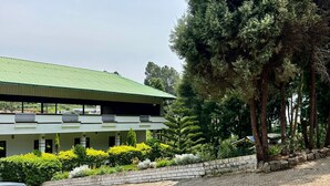 A building with a green roof, surrounded by trees and a paved driveway.