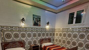 Una habitación tradicional con dos camas, paredes con diseño y una lámpara decorativa en el techo.