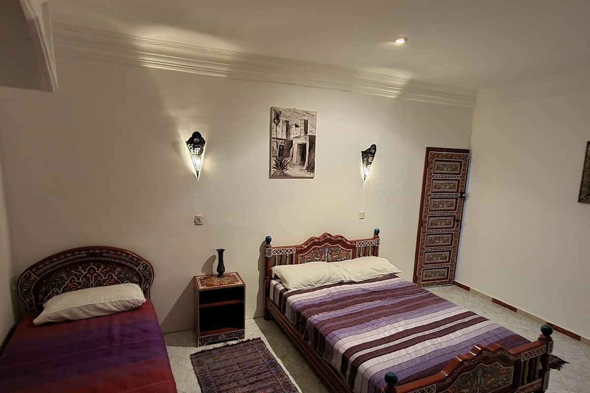 A bedroom with two beds, a nightstand, a rug, and a wall-mounted light fixture.
