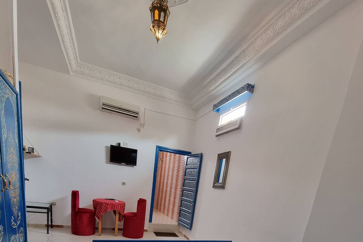 A bedroom with a blue bed, a red chair, a small table, and a decorative wall panel.
