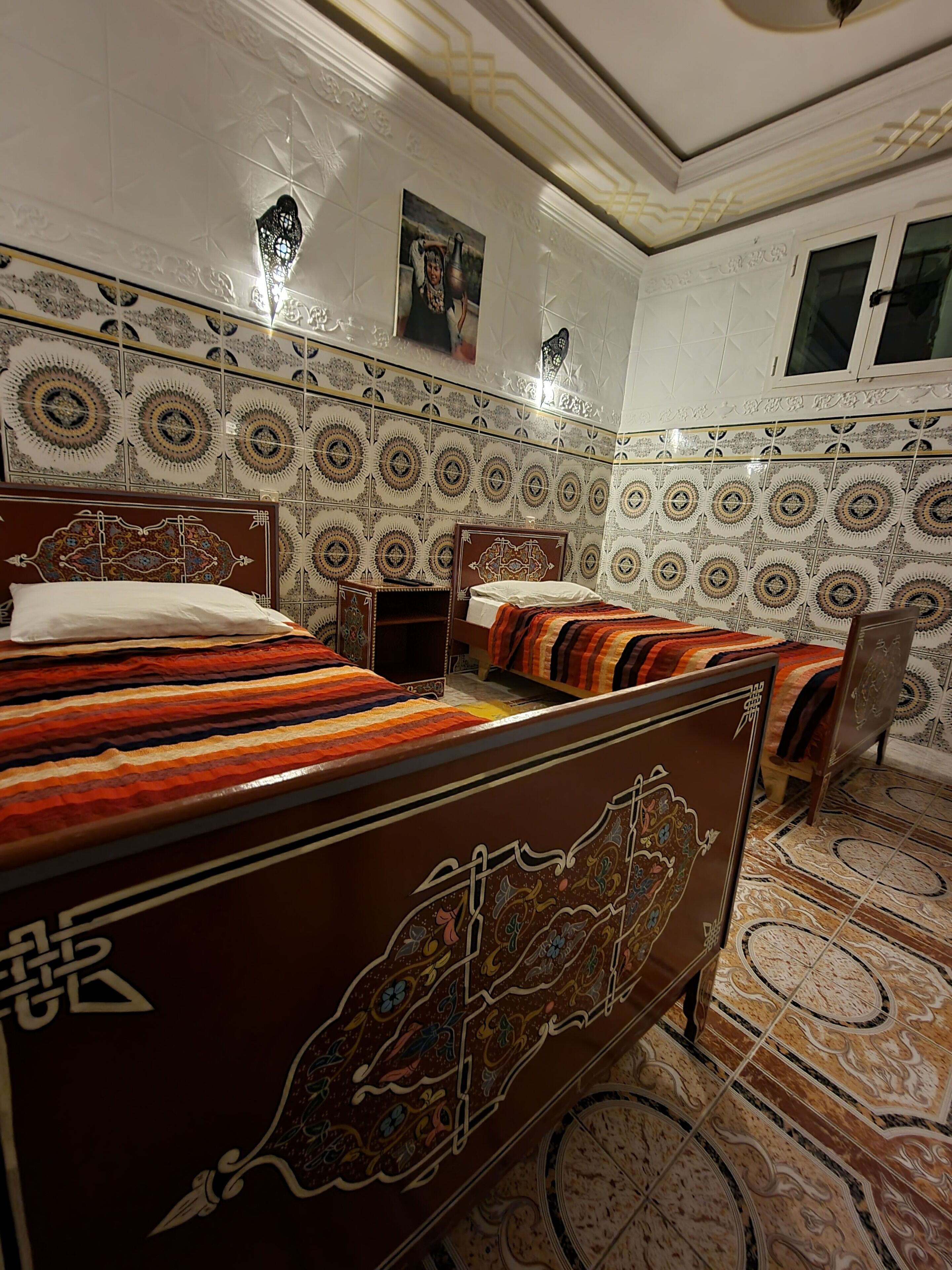 Une chambre de style traditionnel, dotée de deux lits, de carreaux muraux décoratifs et d’un sol à motifs.