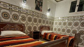 Une chambre de style traditionnel, dotée de deux lits, de carreaux muraux décoratifs et d’un sol à motifs.