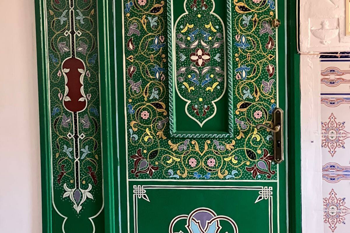 A green door with intricate floral and geometric patterns, a central rectangular design, and a small heart-shaped motif.