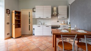 A compact kitchen with white cabinets, a wooden dining table with chairs, and a tiled floor. - Nice apartment for 4 people with WIFI, pool, A/C, terrace, pets allowed and panoramic view (Portacomaro)