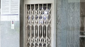 Une porte en métal ornée d’un motif en losanges, un mur sur lequel est fixé un panneau d’affichage et une vue partielle de la façade d’un bâtiment.