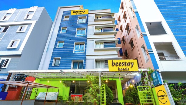 Un hôtel reconnaissable à son panneau bien visible indiquant « beestay hotels », une zone d’entrée verdoyante agrémentée de plantes en pot et un escalier menant à l’entrée.