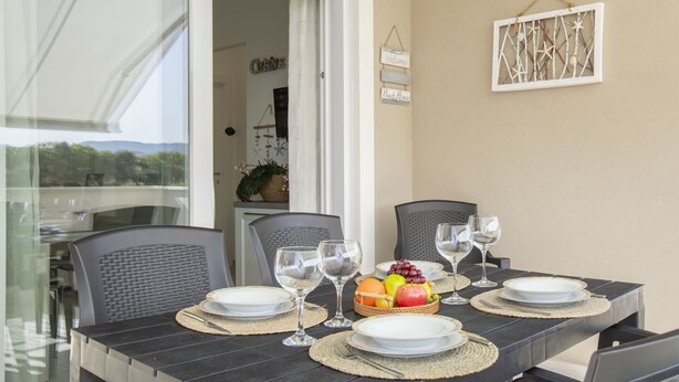 Une table à manger dressée avec des assiettes, des verres et un panier de fruits, entourée de chaises.