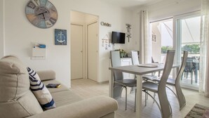 Ein modernes Wohnzimmer mit einer Couch, einem Essbereich mit Tisch und Stühlen, einer Wanduhr und einer Schiebetür zu einem Außenbereich.