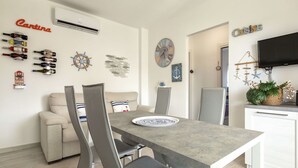 Ein moderner Essbereich mit grauem Tisch und Stühlen, einer weißen Couch und einer Küchenzeile mit Fernseher und Dekorationselementen.