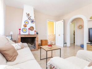 A living room with a fireplace, a sofa, a television, and a door leading to another room.