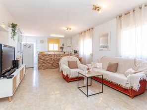 Ein Wohnzimmer mit Fernseher, Sofa, Couchtisch und einer Küche im Hintergrund.