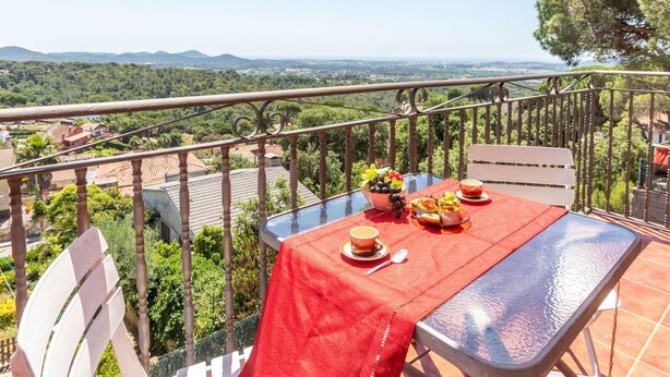 A balcony with a table set for two, a view of the countryside, and a metal railing.