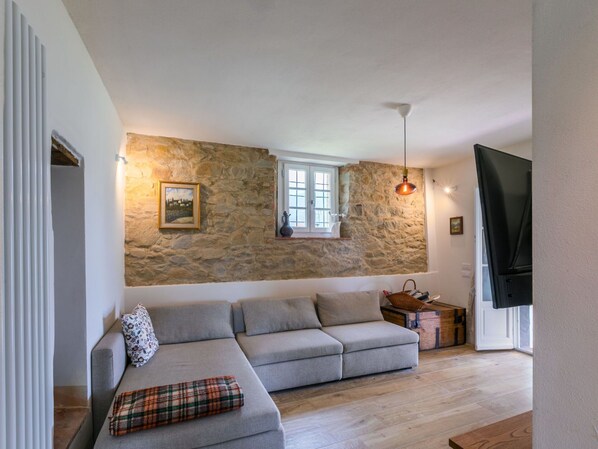 A living room with a stone wall, a grey sofa, a window, and a television. - Wonderful private villa with WIFI, private pool, TV, patio, pets allowed and panoramic view (Pescia)