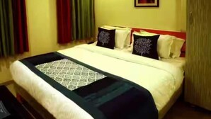 A hotel room with a bed, a desk, and a painting on the wall. - Hotel Royal Apple (Ahmedabad)
