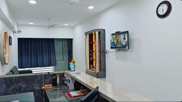 A modern hotel room with a marble reception desk, a large window with curtains, a ceiling fan, and a clock on the wall. - Hotel Royal Apple (Ahmedabad)