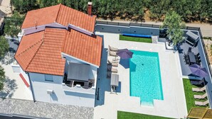 Une maison à deux étages avec un toit recouvert de tuiles rouges, une piscine et un espace salon extérieur.