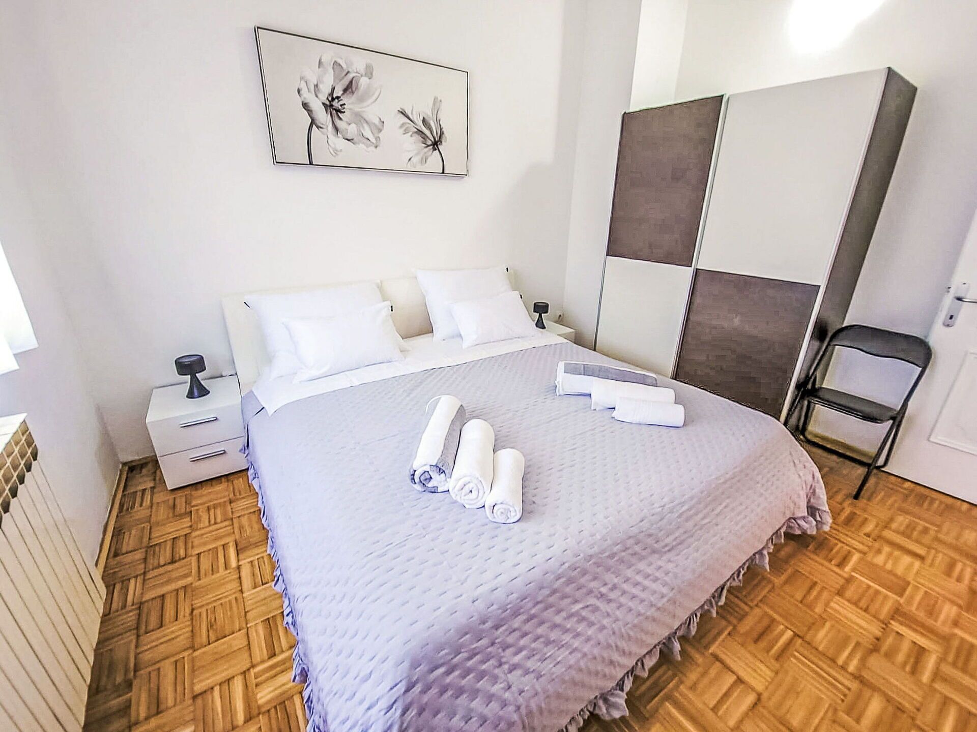 Een keurig opgemaakte hotelkamer met een bed, nachtkastje, stoel en garderobe.
