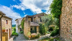 A narrow stone pathway leading to a rustic stone building with a tiled roof, surrounded by lush greenery and flowering plants. - Lovely apartment for 6 guests with WIFI, pool, A/C, TV, patio, pets allowed and panoramic view (Gaiole In Chianti)
