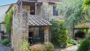 A stone house with a tiled roof, a balcony, and a garden with potted plants. - Lovely apartment for 6 guests with WIFI, pool, A/C, TV, patio, pets allowed and panoramic view (Gaiole In Chianti)