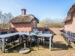 Un bâtiment en briques surmonté d’un toit de chaume, une table de patio avec des chaises et un barbecue.