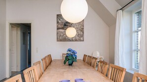 Ein Esszimmer mit einem langen Holztisch, sechs Stühlen, einer Blumenvase und einer großen Pendelleuchte.