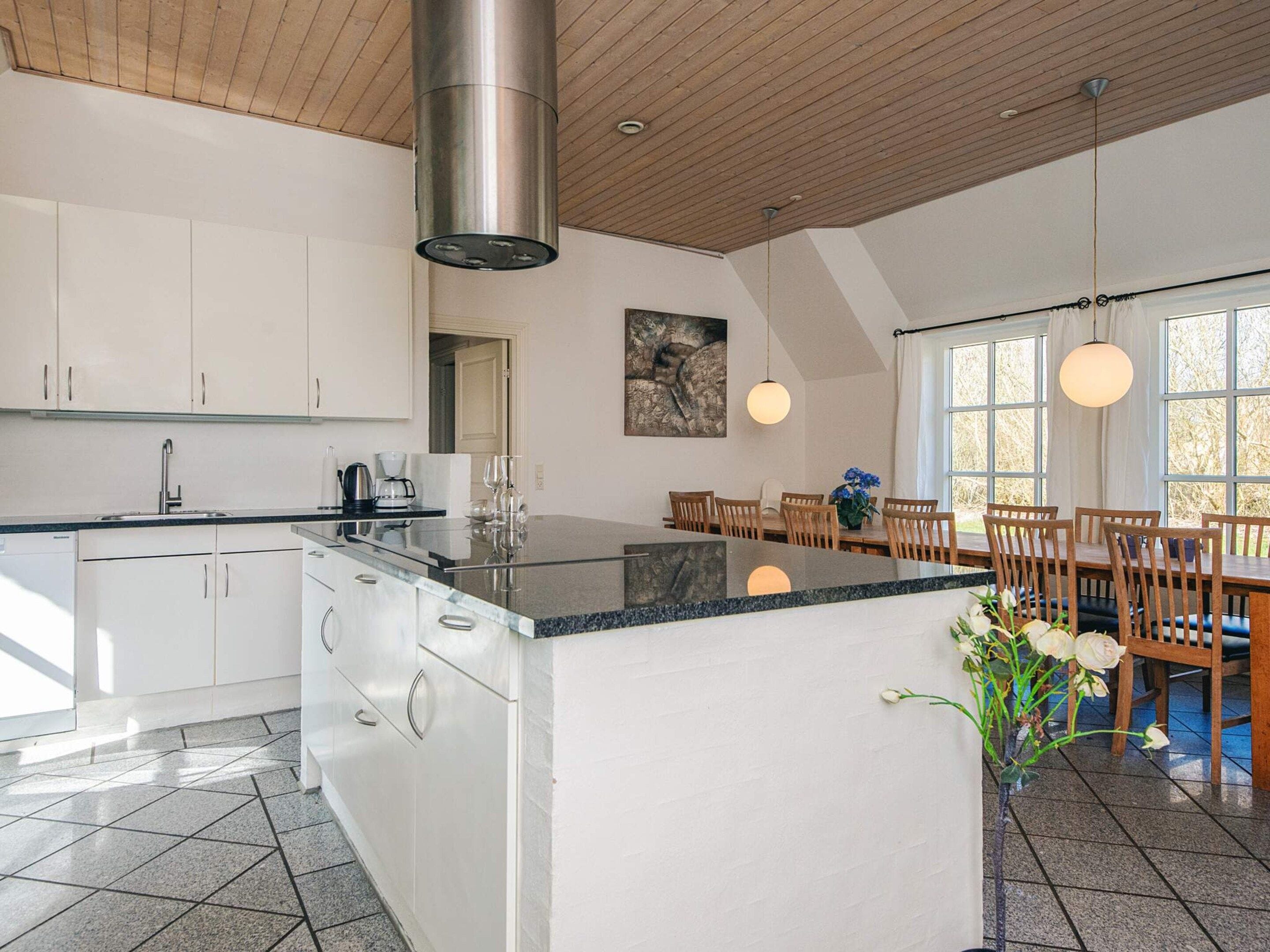 A modern kitchen with white cabinetry, a central island, and a dining area with wooden chairs and a table.