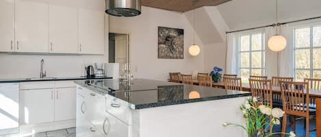 Una cocina moderna con armarios blancos, una isla central y un comedor con sillas y mesa de madera.