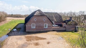 Ein Bauernhaus aus Ziegeln mit Strohdach, Schornstein und einem kleinen Anbau.