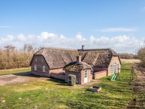 A traditional brick house with a thatched roof, a small attached shed, and a grassy yard with a swing set. - 4 Star Holiday Home in Ulfborg (Ulfborg)