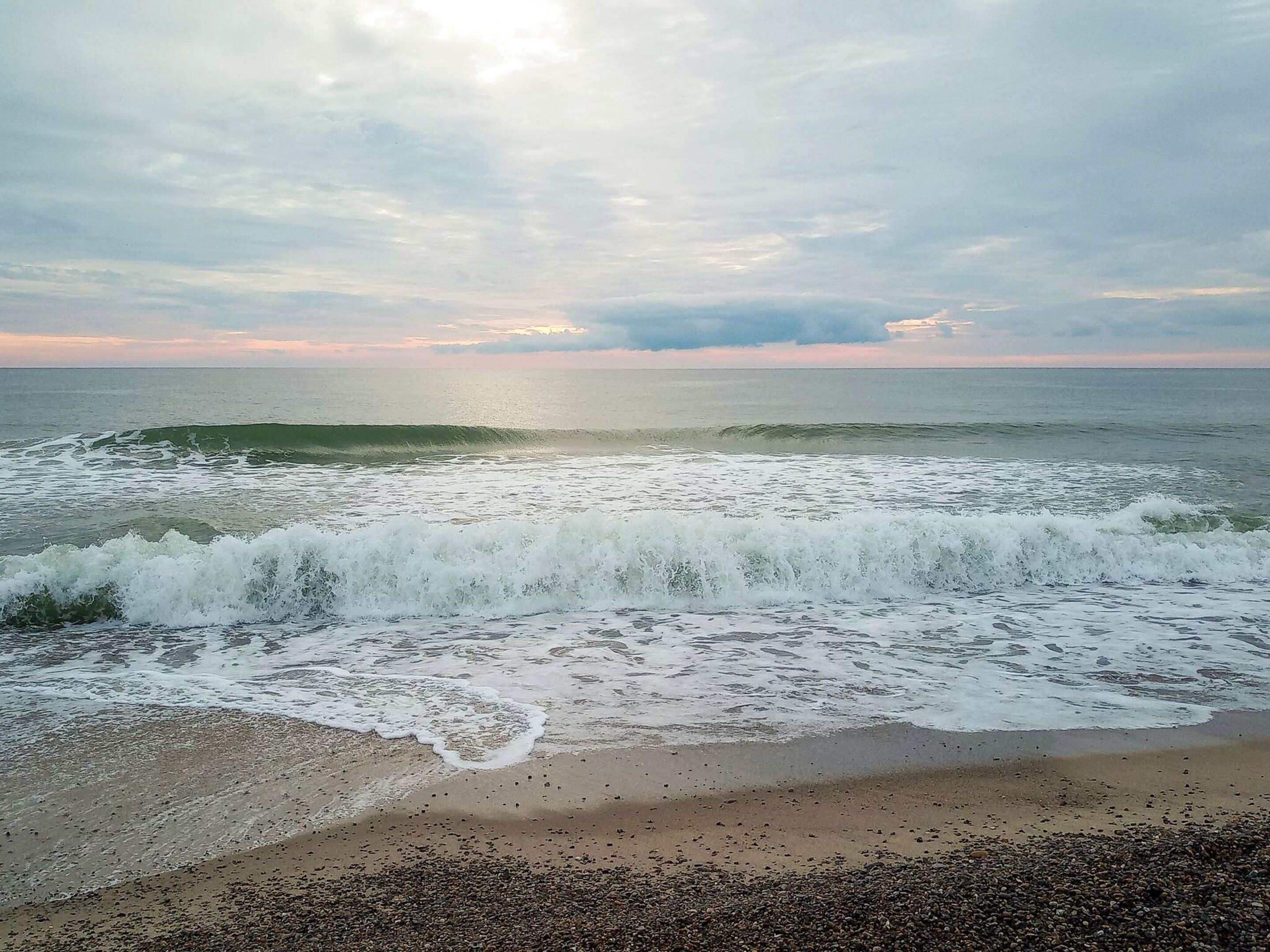 A beach with waves crashing onto the shore and a clear sky.