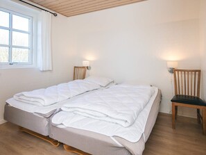 A single bed with a wooden headboard and footboard, two bedside lamps, and a window with white curtains.