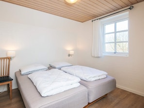 Une pièce avec un lit, une chaise et une fenêtre avec des rideaux.