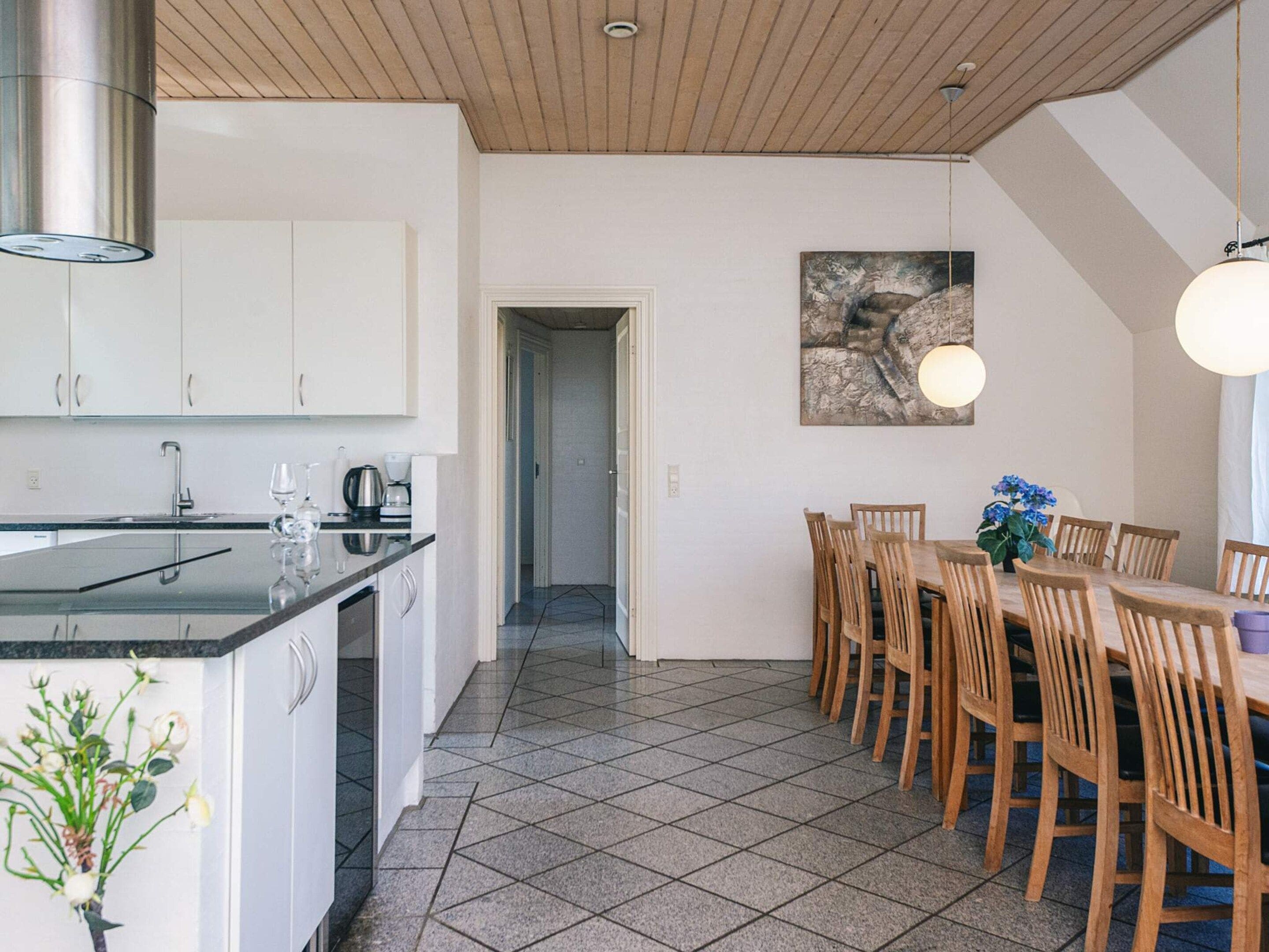 Cozinha moderna com armários brancos, bancada preta e área de jantar com cadeiras e mesa de madeira.