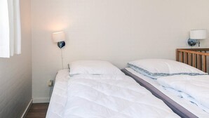 Ein Zimmer mit zwei Betten, einem Holz-Kopfstück, einer Wandlampe und einer Steckdose.