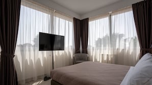 A hotel room with a large bed, a flat-screen TV, a chair, and sheer curtains. - Hotel Bulà (Bollate)