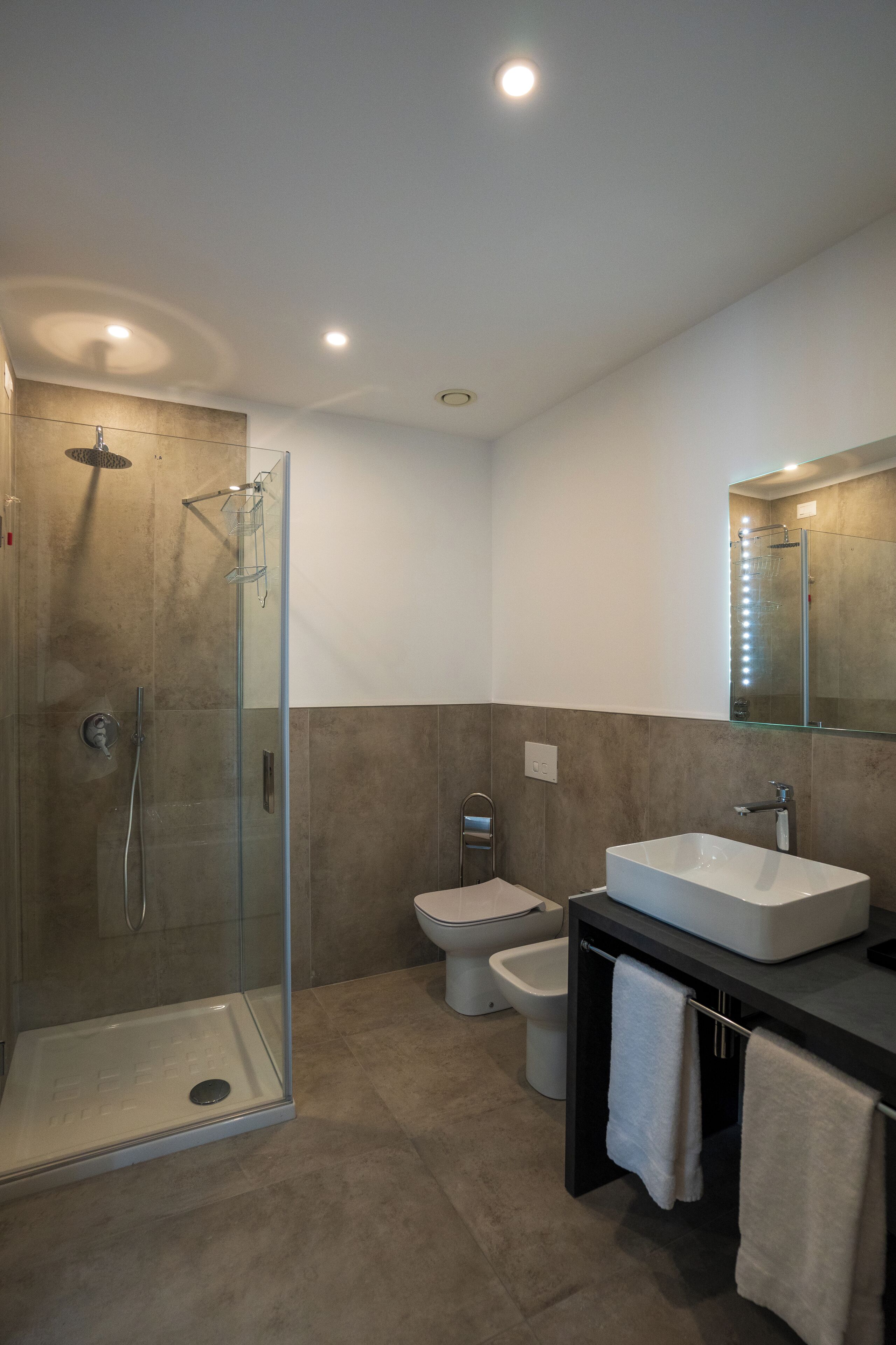 Un baño moderno con ducha de vidrio, lavamanos blanco y un espejo grande.