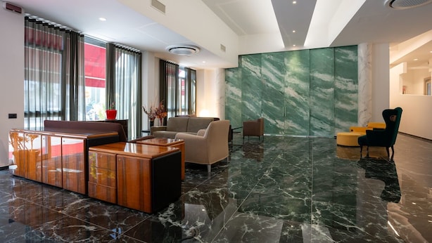 A modern lobby with a reception desk, seating area, and a marble wall. - Hotel Bulà (Bollate)