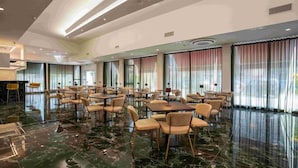 A spacious dining area with marble flooring, large windows with curtains, and multiple tables and chairs. - Hotel Bulà (Bollate)