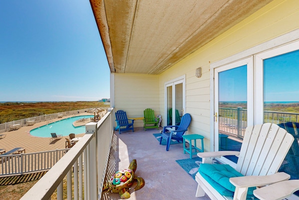 A balcony with a pool, chairs, and a view of the landscape.