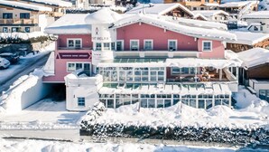 En byggnad med flera våningar och en röd fasad, ett spaområde med en skylt och utsikt över snötäckta berg.
