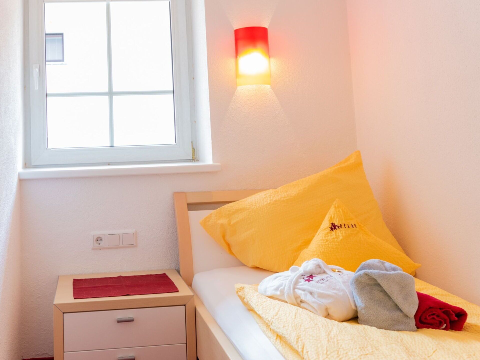 Une chambre à coucher comprenant un lit, une table de chevet, une fenêtre et une lampe fixée au mur.