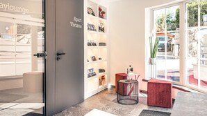 Un intérieur moderne avec une porte grise portant l’inscription « Apart Viviana », une porte vitrée donnant sur l’extérieur et un banc rouge rembourré.
