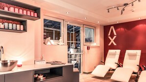 Une salle de spa moderne comprenant un comptoir d’accueil, des étagères avec des bougies, un grand miroir et deux fauteuils de massage.
