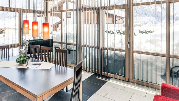 Un espace de salle à manger moderne, doté d’une grande table, de chaises et offrant une vue sur un paysage enneigé grâce à de larges fenêtres.