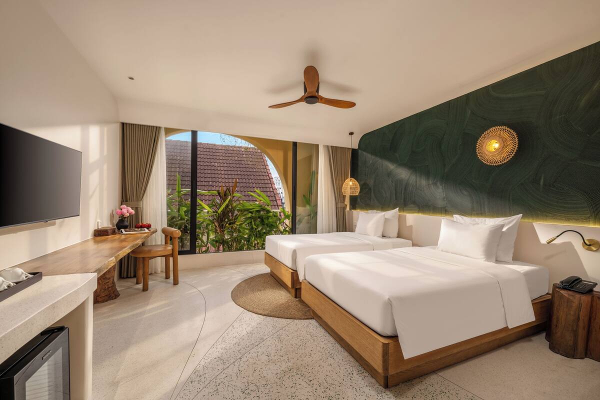 A modern hotel room with a large bed, a desk, a TV, and a balcony with plants.