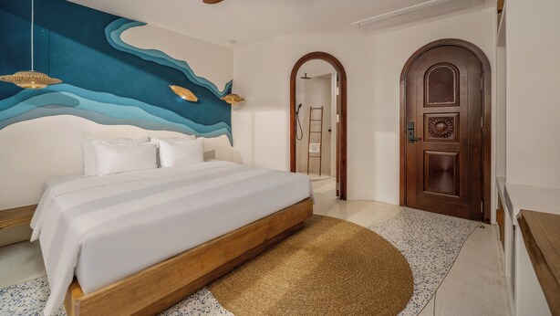A bedroom with a large bed, a ceiling fan, a wall mural, and a wooden door. - Saha Casa Boutique Hotel Da Nang (Da Nang)